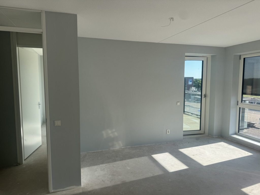Lege nieuwbouwkamer met een betonvloer en afgewerkte lichtgrijze wanden, kort na de oplevering