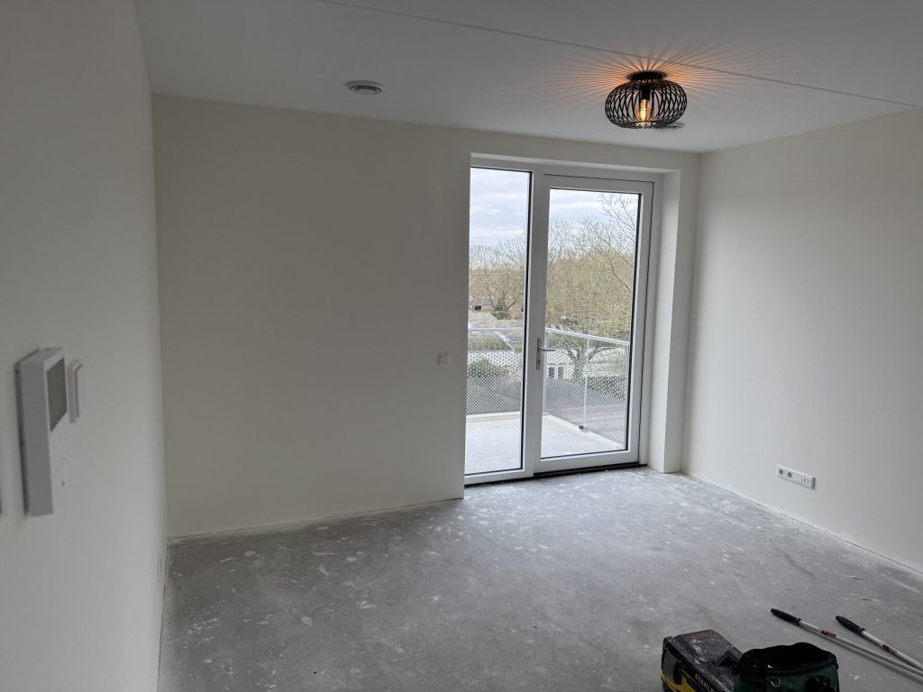 Lege nieuwbouwkamer met strakke witte wanden en openslaande deuren naar een balkon